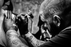 Tattoo artist in black gloves applying a tattoo to a client’s shoulder with a tattoo machine, close-up of hands and ink lines in progress.